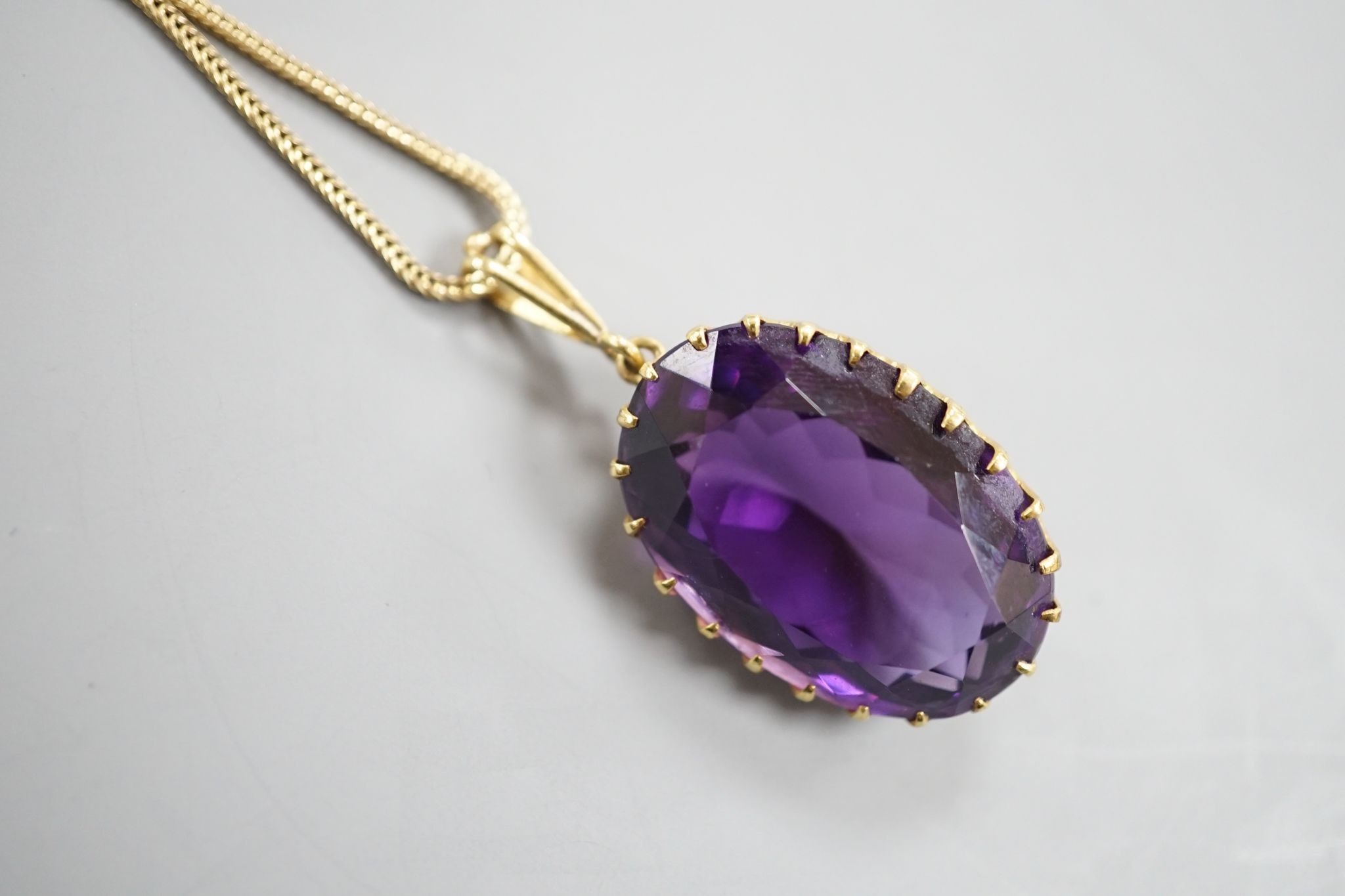 An early 20th century yellow metal mounted oval cut amethyst pendant, overall 37mm, on a yellow metal fine link chain, 49cm, gross weight 10.3 grams.